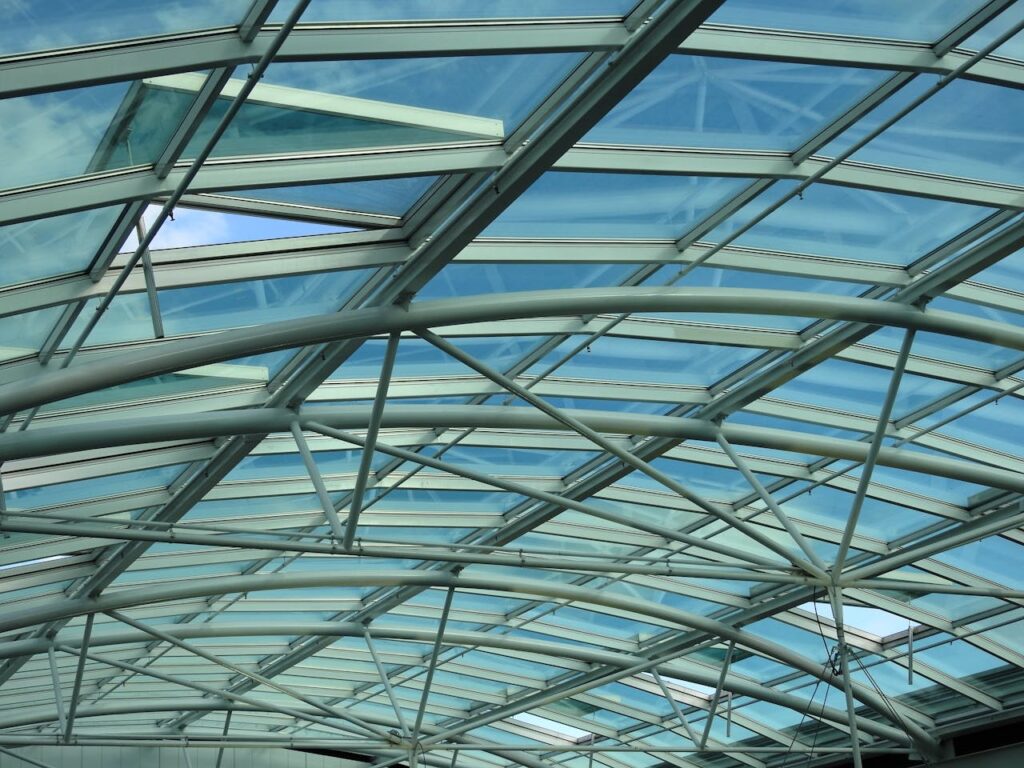 Intricate modern glass ceiling structure with blue sky visible through clear panels, highlighting architectural design.